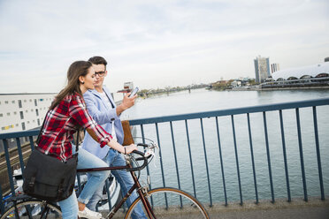 Germany, Mannheim, young man and woman with bicycle and cell phone on bridge - UUF003914