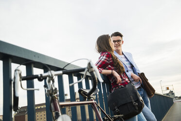 Young man and woman with bicycle on bridge - UUF003916