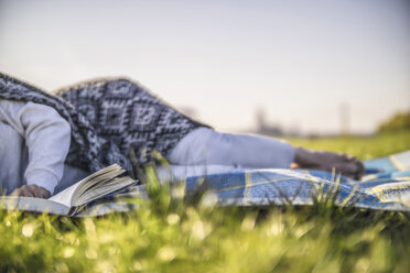 Nahaufnahme einer Frau, die auf einer Decke auf einer Wiese ein Buch liest - RIBF000047