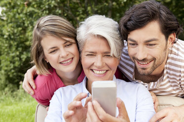 Mother with adult children looking at cell phone outdoors - MFRF000161