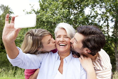 Glückliche Mutter mit erwachsenen Kindern, die ein Handyfoto im Freien machen, lizenzfreies Stockfoto