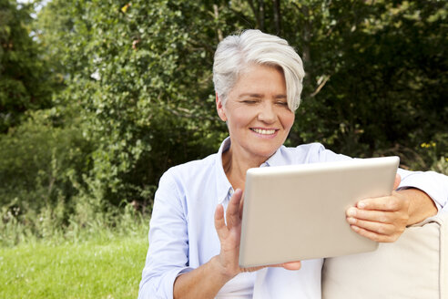 Smiling mature woman outdoors using digital tablet - MFRF000163