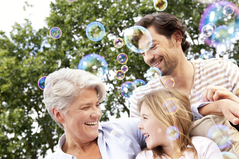 Happy grandmother, father and girl surrounded by soap bubbles - MFRF000170