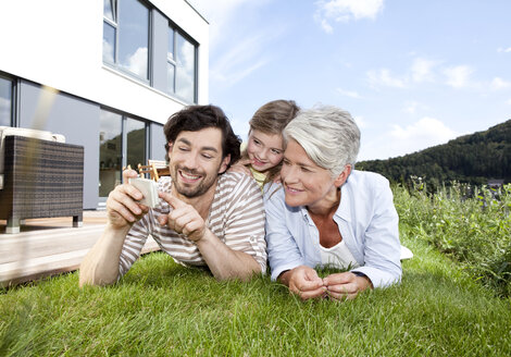 Happy grandmother, father and girl lying on lawn using cell phone - MFRF000175
