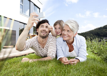 Happy grandmother, father and girl lying on lawn using cell phone - MFRF000176