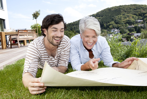 Erwachsener Sohn und Mutter liegen auf dem Rasen und betrachten einen Bauplan, lizenzfreies Stockfoto