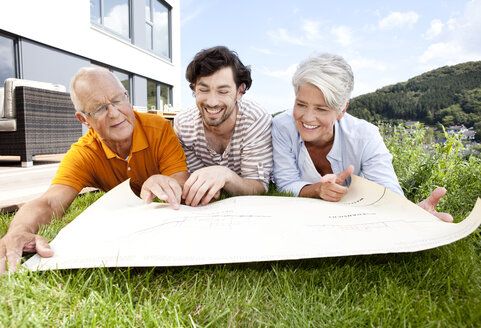 Adult son and parents lying on lawn looking at construction plan - MFRF000178