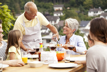 Grandfather serving food from barbecue grill for family at garden table - MFRF000204