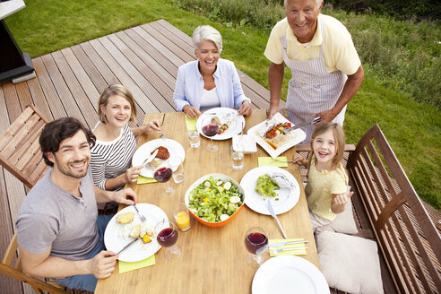 Grandfather serving food from barbecue grill for family at garden table - MFRF000183