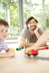 Vater liegt auf dem Boden und beobachtet Kinder, die mit einer Spielzeugeisenbahn spielen - MFRF000187