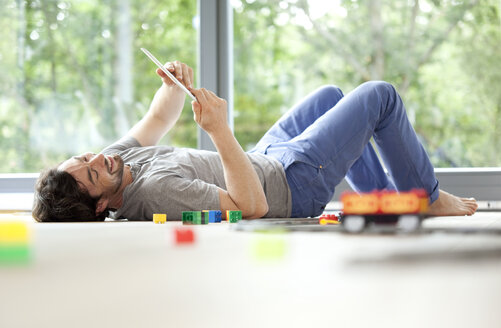 Smiling man lying on floor with digital tablet next to toy train - MFRF000188