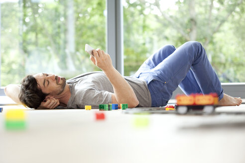 Man lying on floor with cell phone next to toy train - MFRF000189