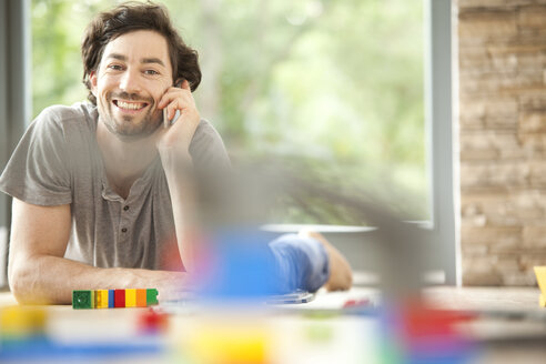 Smiling man on cell phone lying on floor next to toy train - MFRF000191