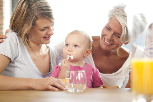 Grandmother and mother looking at baby girl eating yogurt - MFRF000331