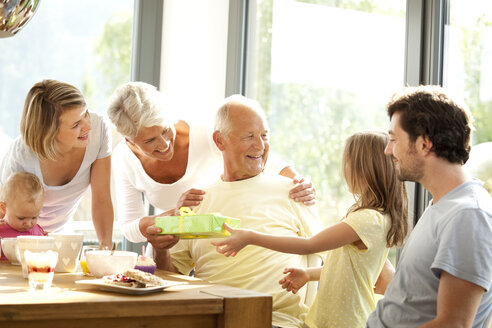 Senior man receiving present from his granddaughter at breakfast table - MFRF000210