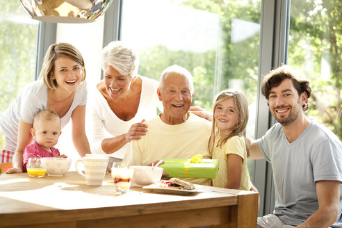 Portrait of happy extended family with present at breakfast table - MFRF000211