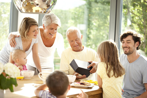 Glückliche Großfamilie mit Geschenk am Frühstückstisch - MFRF000212