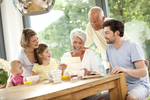 Glückliche Enkelin mit ihrer Familie beim Lesen eines Briefes am Frühstückstisch, lizenzfreies Stockfoto