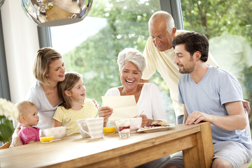 Happy granddaughter with her family reading letter at breakfast table - MFRF000213