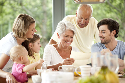 Glückliche Enkelin mit ihrer Familie beim Lesen eines Briefes am Frühstückstisch - MFRF000214