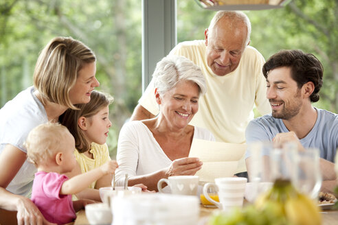 Happy granddaughter with her family reading letter at breakfast table - MFRF000214