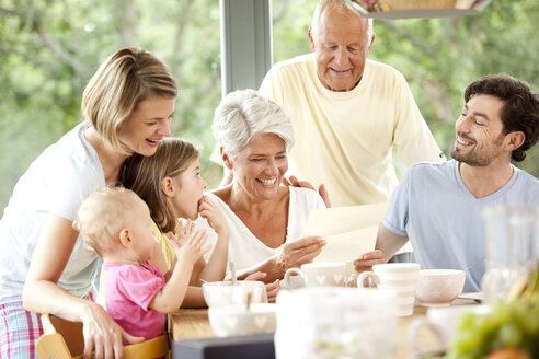 Glückliche Enkelin mit ihrer Familie beim Lesen eines Briefes am Frühstückstisch - MFRF000215