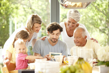 Vater mit seiner Familie beim Lesen einer Postkarte am Frühstückstisch - MFRF000216