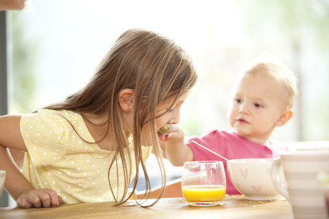 Baby-Mädchen füttert Schwester am Frühstückstisch, lizenzfreies Stockfoto