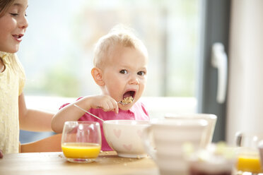 Baby girl eating muesli at breakfast table - MFRF000220