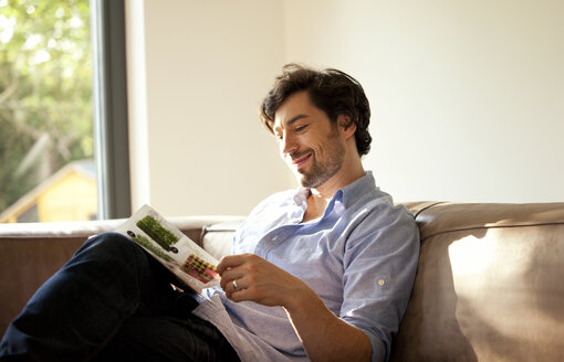 Man sitting on couch reading catalogue - MFRF000198