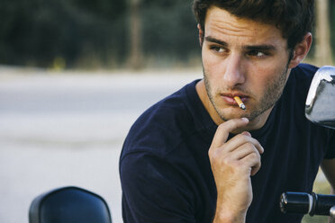 Young man smoking sitting on his motorbike - ABZF000028