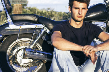 Spain, Madrid, young man sitting next to his motorbike at sunset - ABZF000025