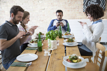 Freunde sitzen zusammen am Esstisch und posten Essen - FKF000996