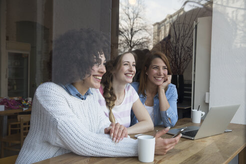 Glückliche Freundinnen mit Laptop und Mobiltelefon in einem Café - FKF001008