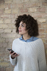 Porträt einer jungen Frau mit Mobiltelefon an einer Backsteinmauer - FKF000973