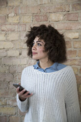 Portrait of young woman with cell phone at brick wall - FKF000973