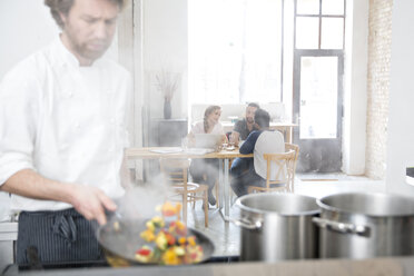 Koch bei der Arbeit in der Küche seines Restaurants, während die Gäste im Hintergrund kommunizieren - FKF001048