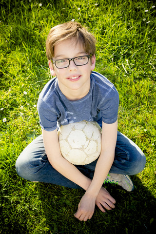 Porträt eines Jungen, der mit einem Fußball auf einer Wiese sitzt, lizenzfreies Stockfoto