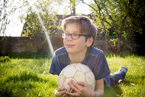 Porträt eines auf einer Wiese liegenden Jungen mit Fußball, lizenzfreies Stockfoto