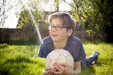 Porträt eines auf einer Wiese liegenden Jungen mit Fußball - LVF003257