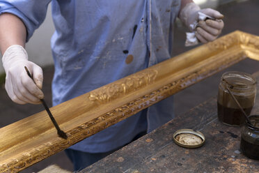 Rahmenmacher in der Werkstatt beim Patinieren eines barocken Holzrahmens - TCF004644