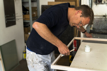 Frame-maker in workshop painting a wooden frame - TCF004646