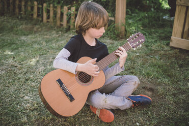 Little boy sitting in the garden playing acoustic guitar - RAEF000158