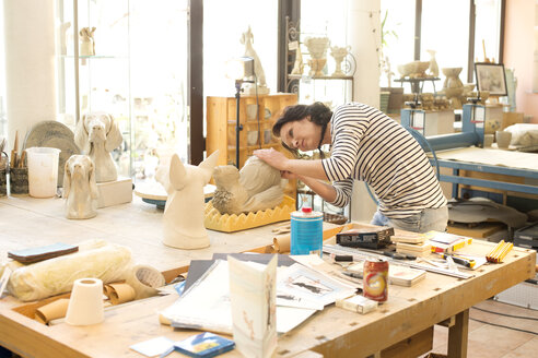 Töpfer in der Werkstatt bei der Arbeit an einer Hundefigur - MAEF010379