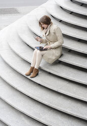 Germany, Berlin, Young businesswoman with digital tablet and smartphone sitting on steps - BFRF001124