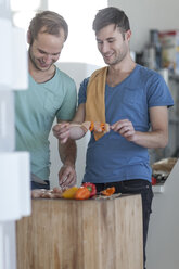 Happy gay couple preparing meat skewers in kitchen - ZEF004466