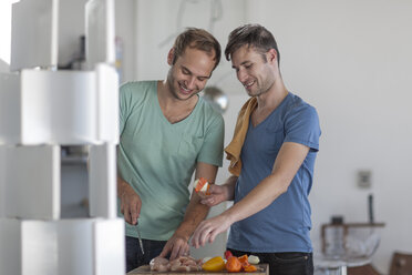 Happy gay couple preparing meat skewers in kitchen - ZEF004467