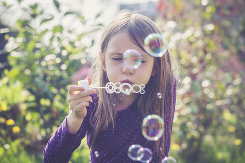 Girl blowing soap bubbles in a garden - SARF001753