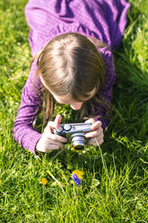Little girl lying on meadow photographing a flower - SARF001791