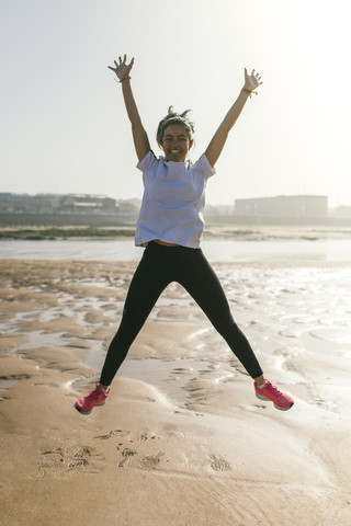 Spanien, Gijon, glückliche junge Frau springt am Strand, lizenzfreies Stockfoto